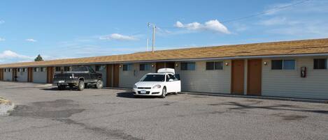 A motel with a row of rooms, a parking lot, and a building with a wooden roof.