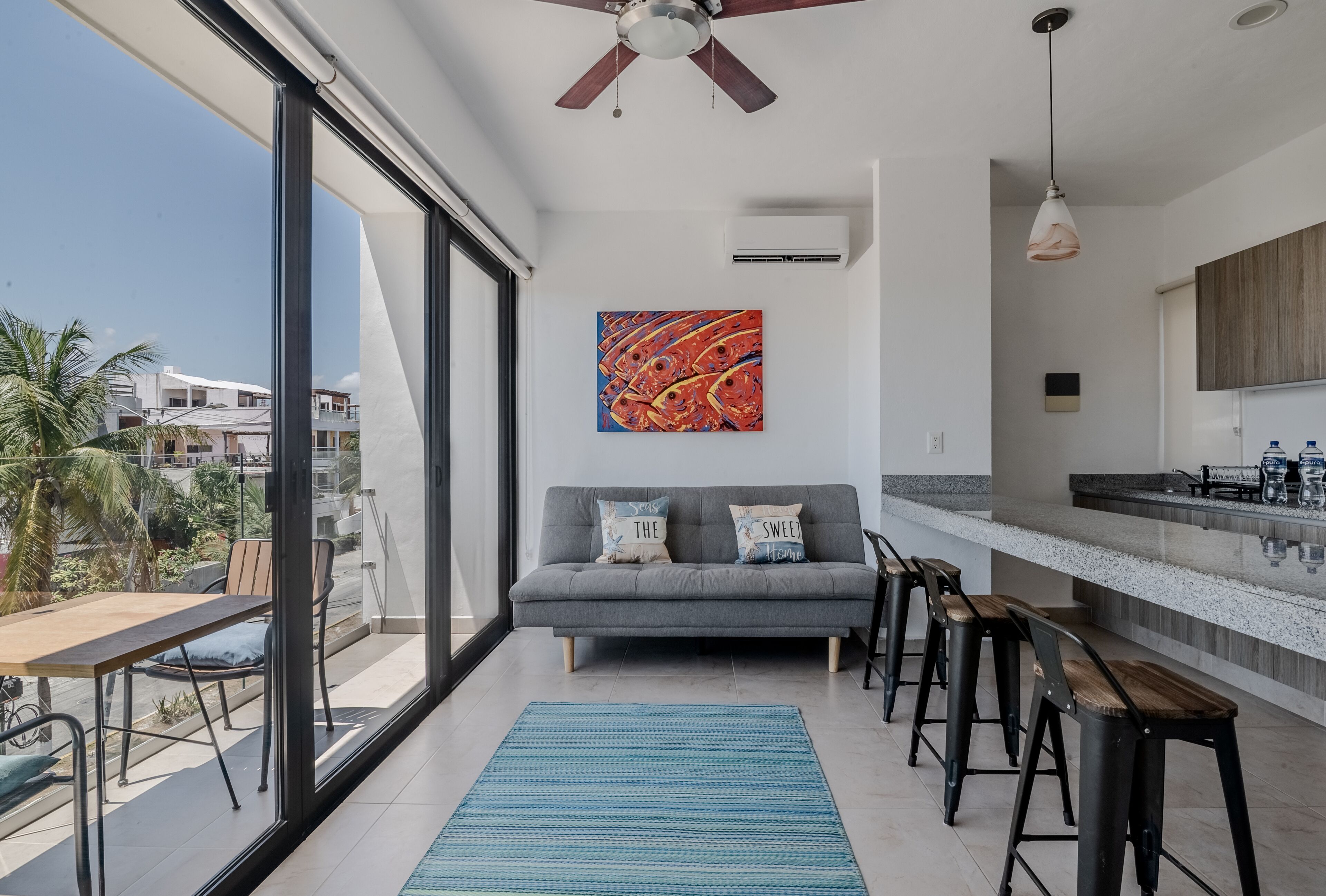 Uma sala de estar moderna com um sofá cinzento, um tapete azul e uma janela grande com vista para a cidade.
