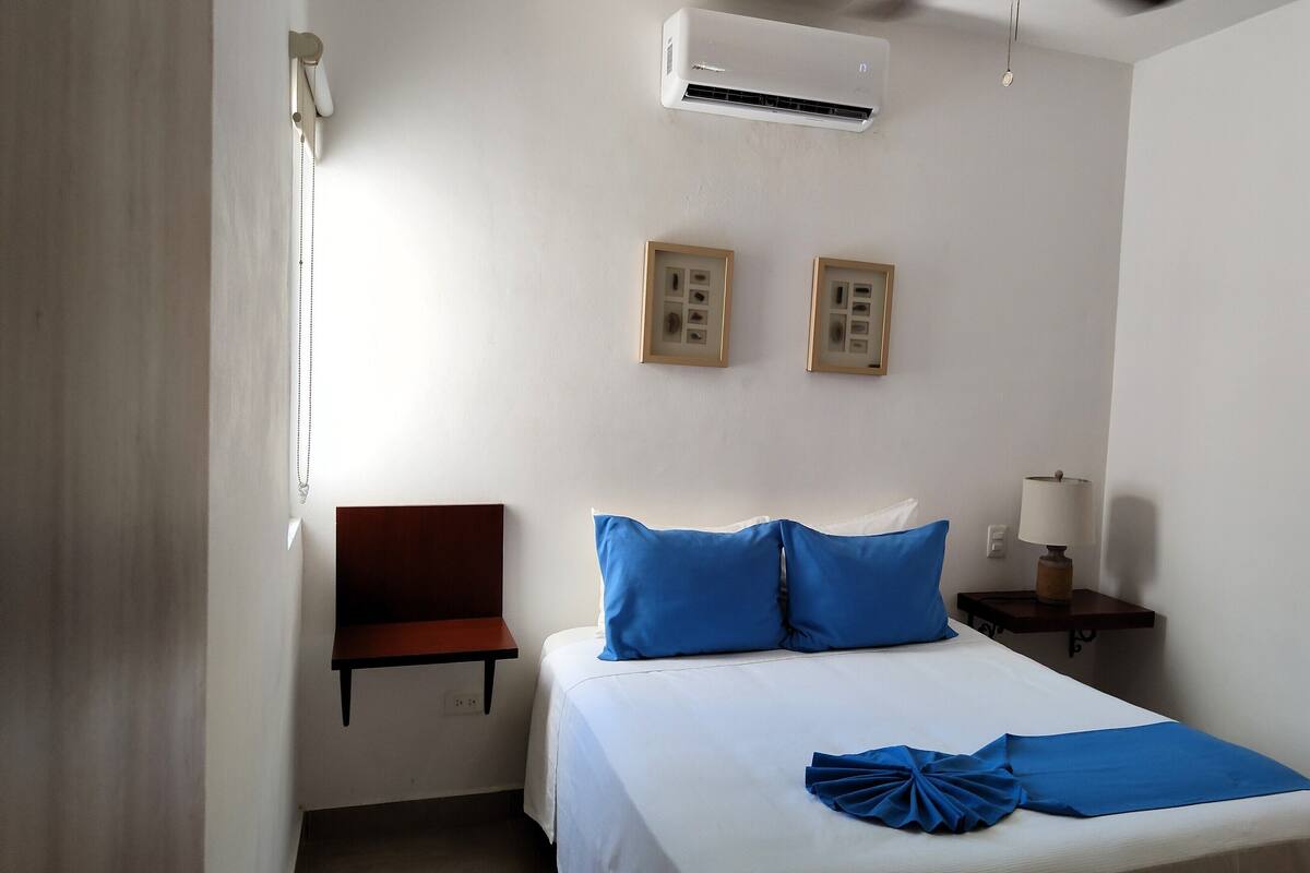 Habitación de hotel con cama, una silla, una mesita de noche y un equipo de aire acondicionado.