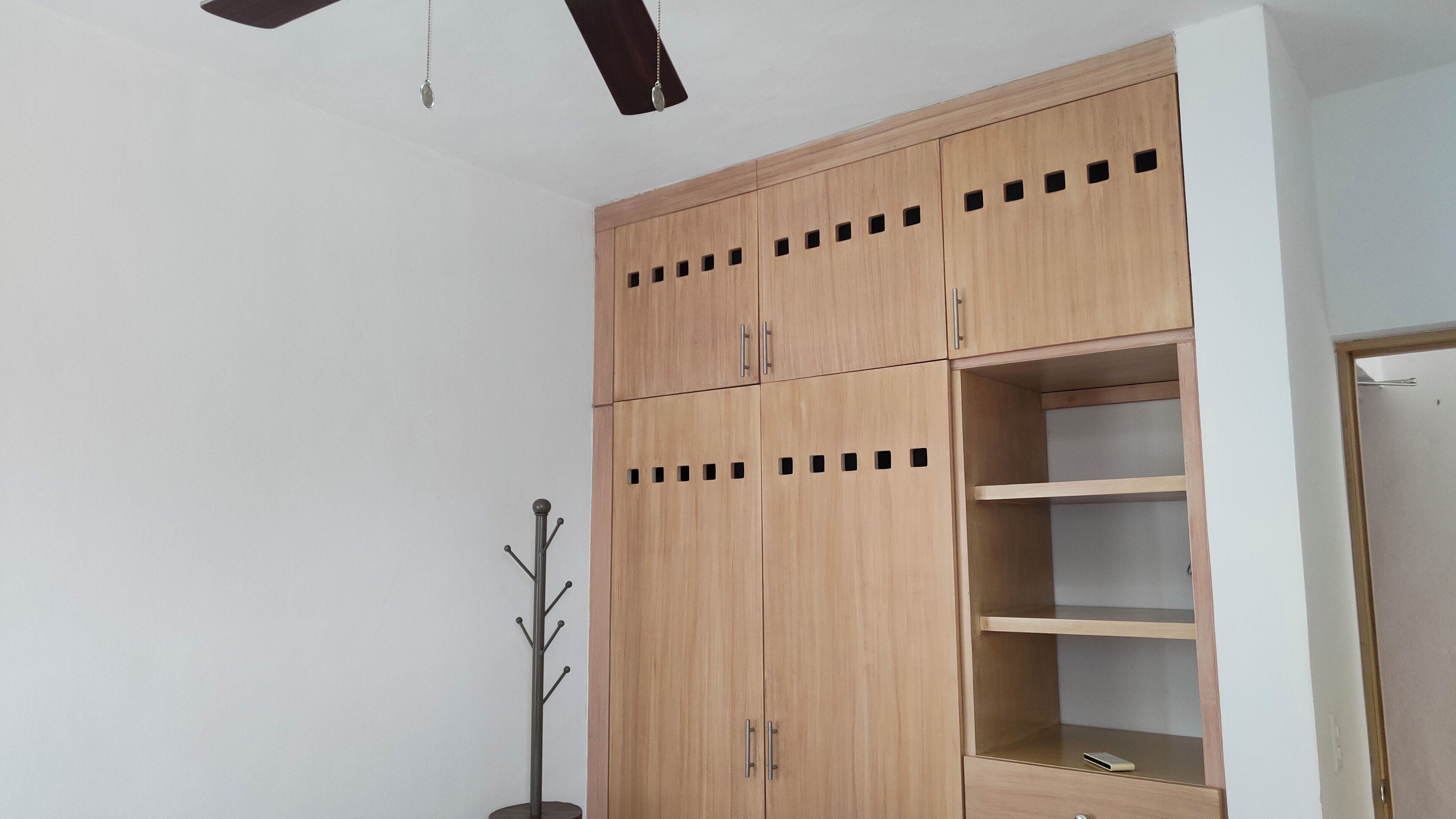 Habitación con un armario de madera con varias puertas y estantes, un perchero y un ventilador de techo.