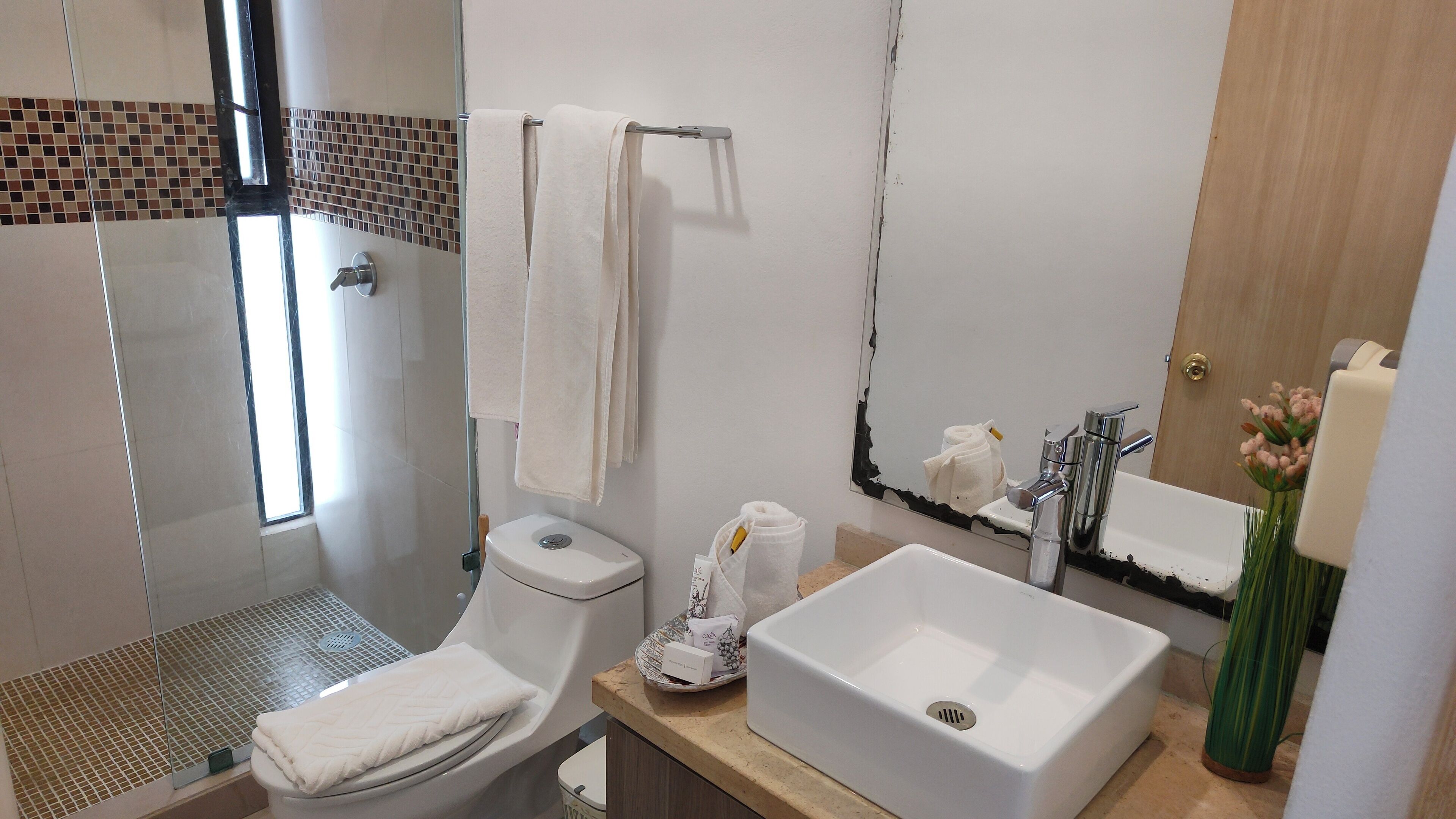 A bathroom with a shower, toilet, sink, and a mirror.