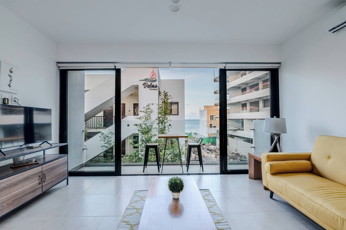 Una sala moderna con un sofá, un televisor y un balcón con una mesa y sillas.