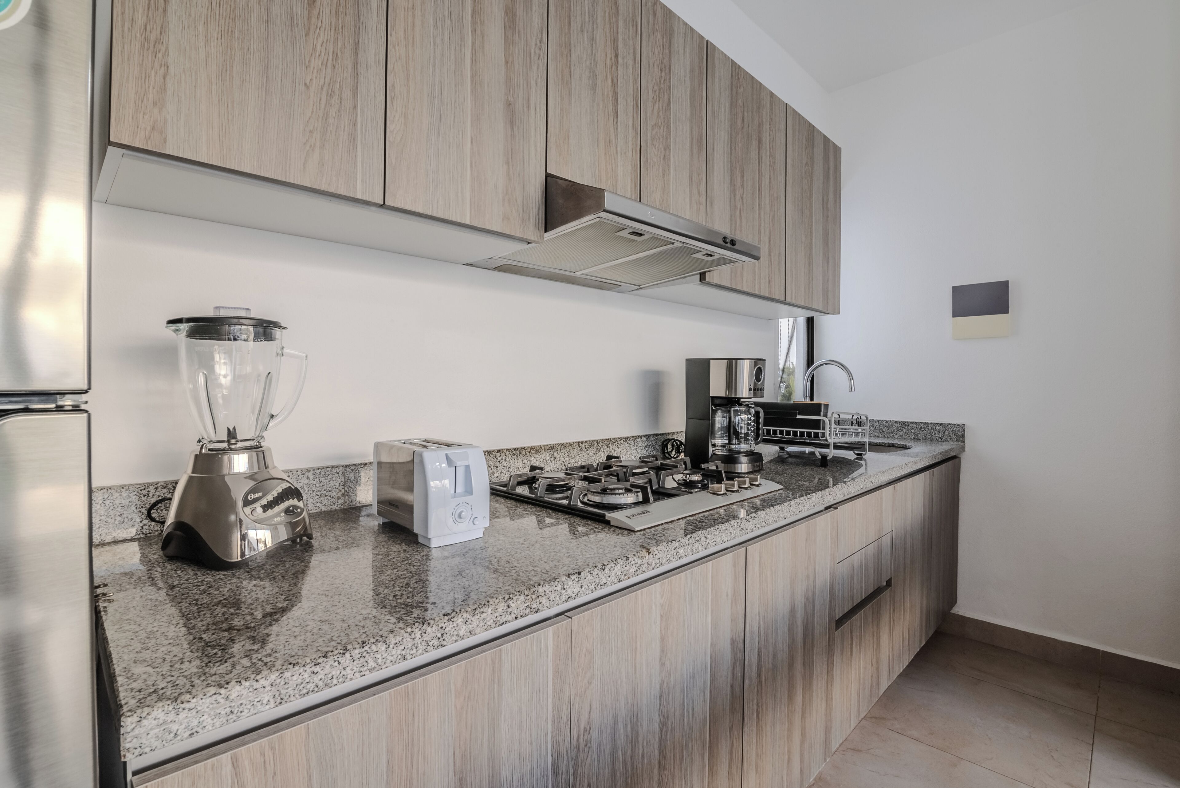 A modern kitchen with wooden cabinets, a granite countertop, a built-in gas stove, a blender, and a toaster.