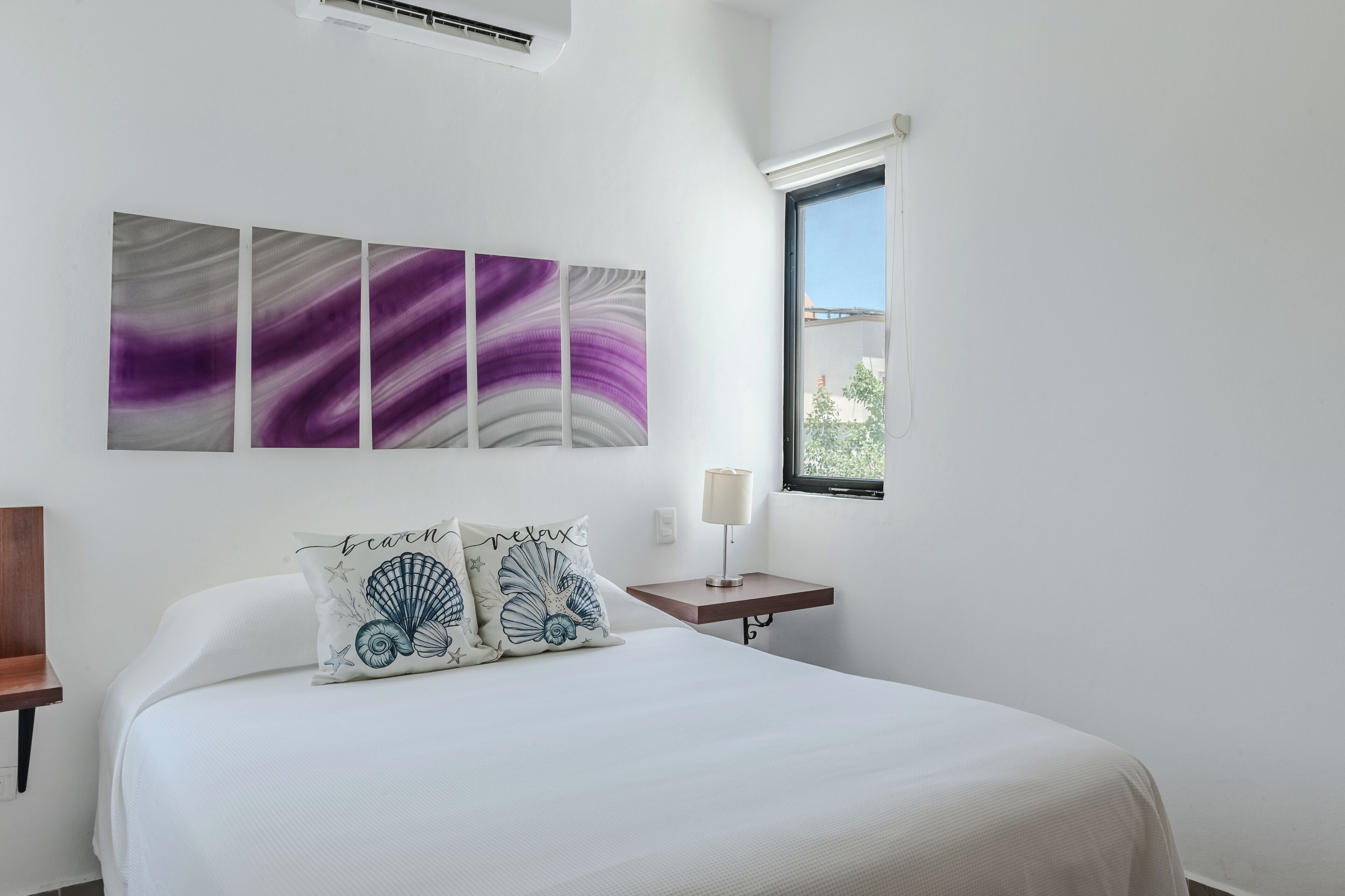 Une chambre à coucher avec un lit, une table de chevet, une lampe fixée au mur et une fenêtre donnant sur un beau paysage.