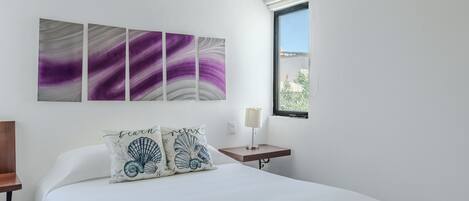 Une chambre à coucher avec un lit, une table de chevet, une lampe fixée au mur et une fenêtre donnant sur un beau paysage.