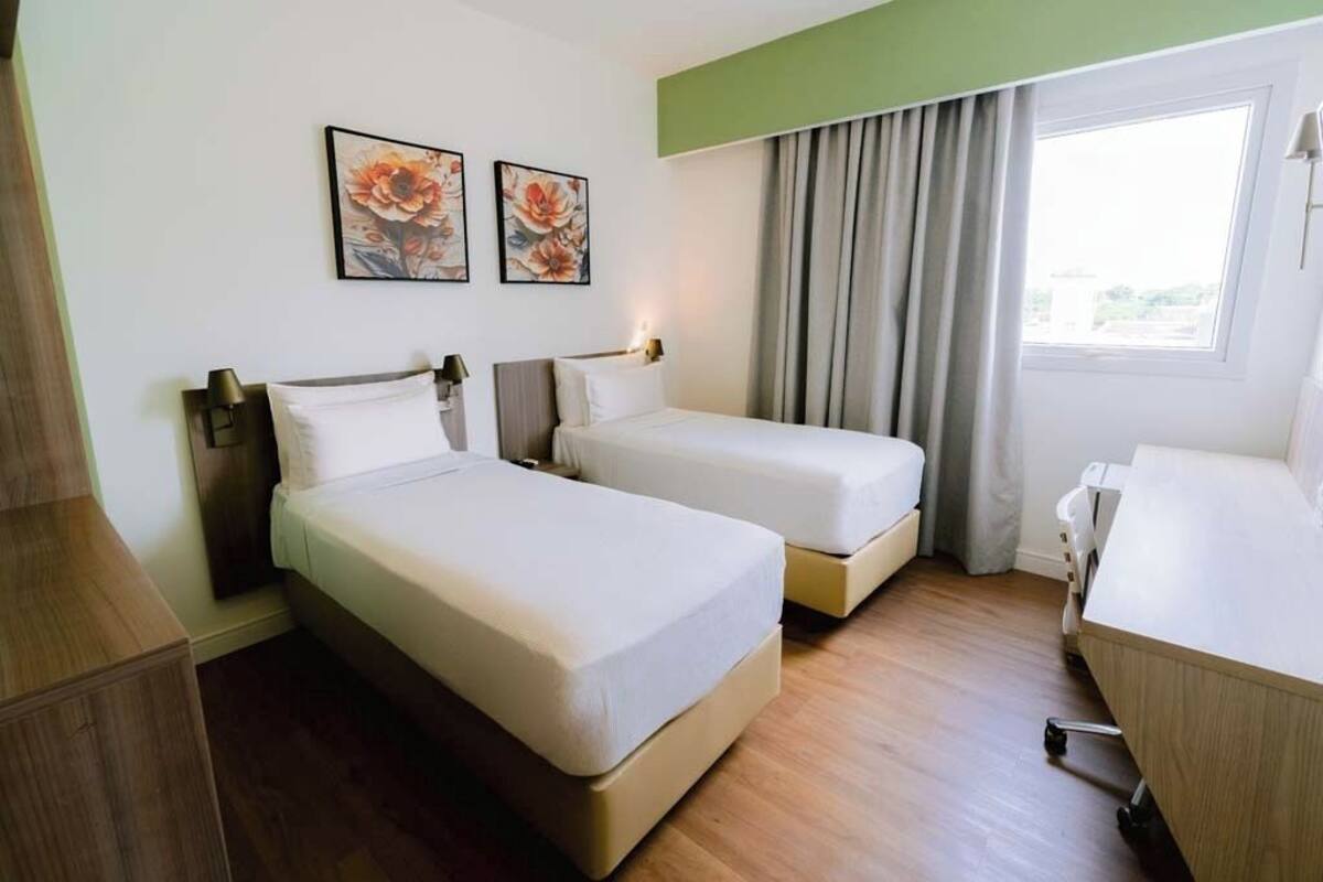 Une chambre d’hôtel avec deux lits simples, un bureau et une fenêtre avec des rideaux.