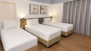 Habitación de hotel con tres camas individuales, suelo de madera, una puerta y dos lámparas fijadas a la pared.