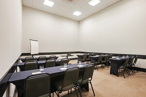 Una sala de conferencias con una larga mesa, sillas, una pizarra y una pantalla para proyector.