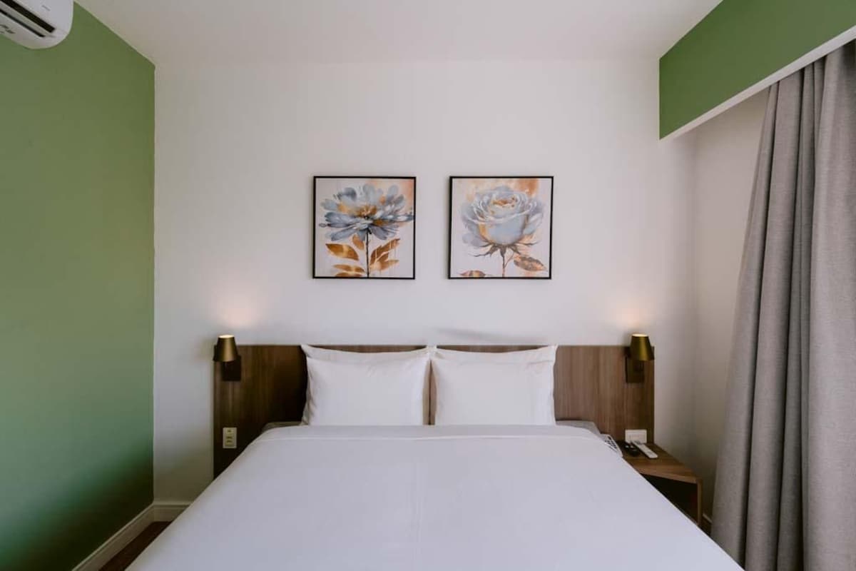 A hotel room with a bed, two wall-mounted lamps, and two framed floral paintings.
