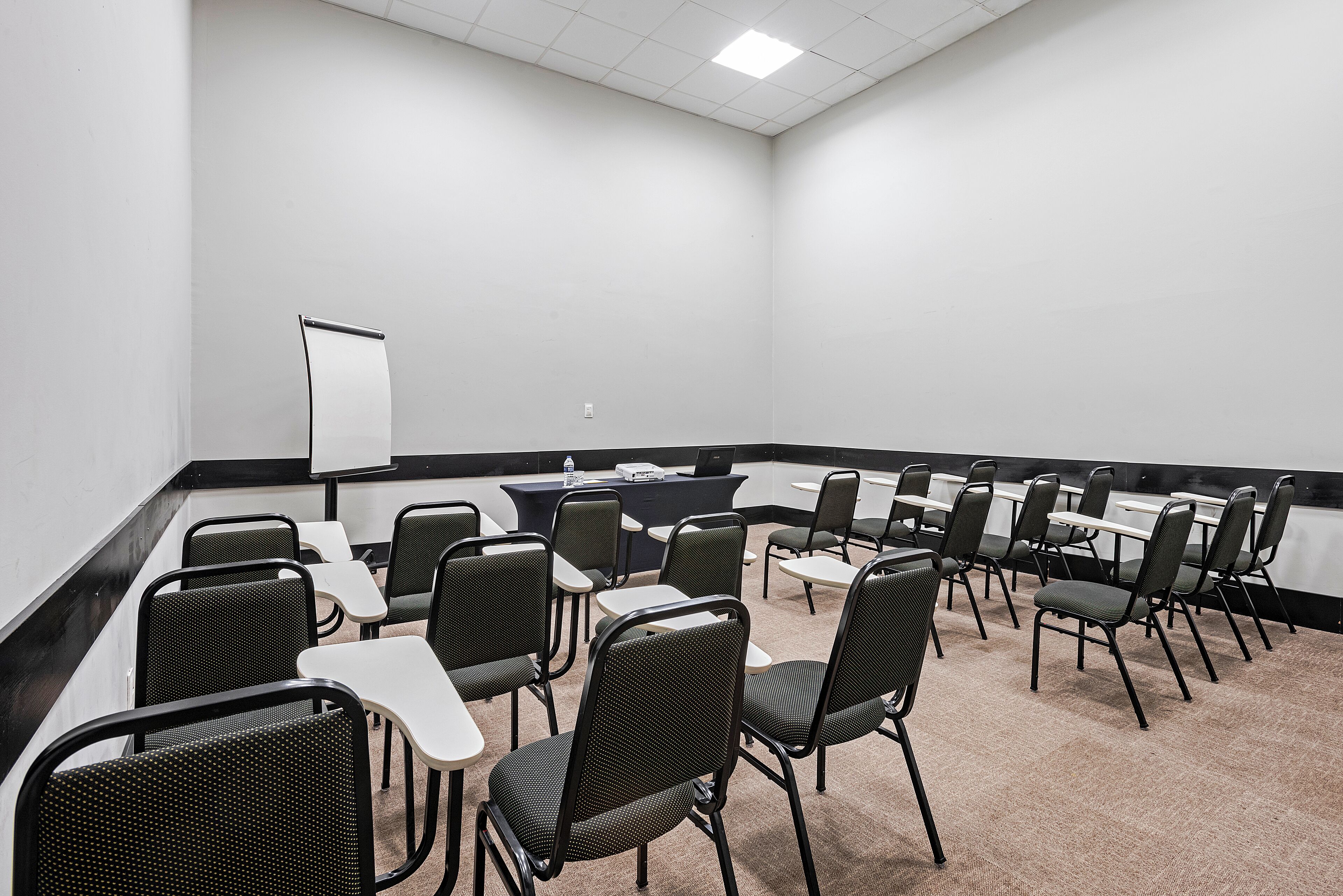 Une salle de conférence équipée d’un tableau blanc, d’un ordinateur portable et de plusieurs chaises disposées autour de tables.