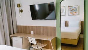 Una habitación de hotel con cama, escritorio, silla, televisor y un refrigerador pequeño.