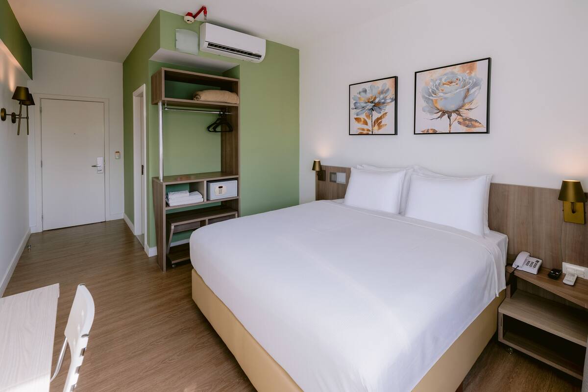 Une chambre d’hôtel avec un grand lit, une armoire, un bureau avec une chaise et deux tableaux au mur.