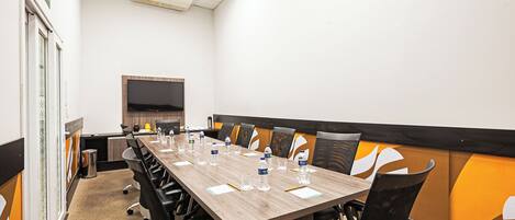 A conference room with a long table, chairs, and a large screen.