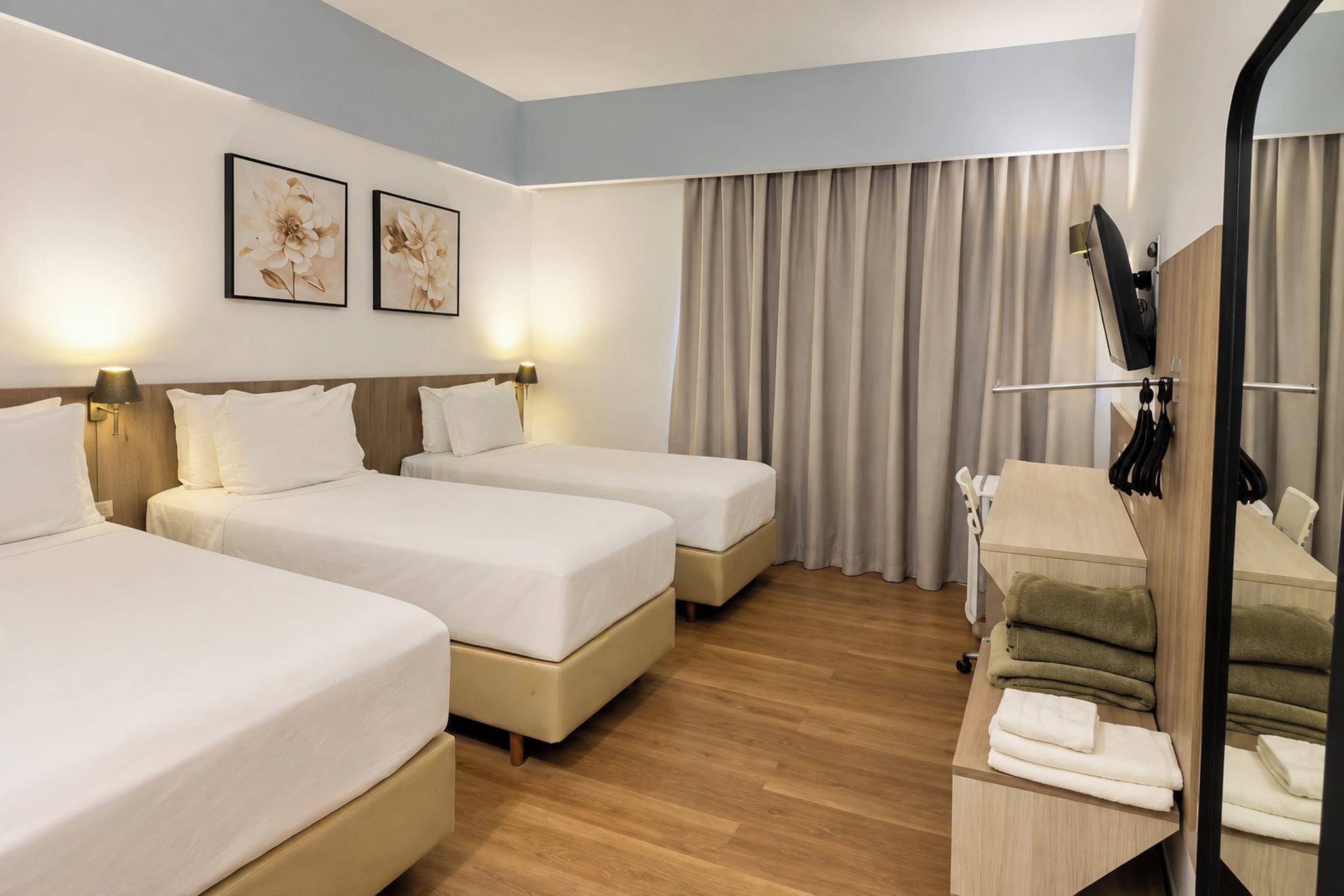 Habitación de hotel con dos camas, un sofá, un espejo y una ventana con cortinas.