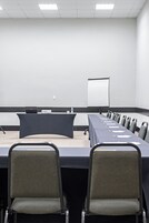 Un salón de conferencias con una larga mesa, sillas, un proyector y una pizarra.