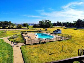 A swimming pool surrounded by a fenced area with a grassy lawn, a small shed, and a paved walkway.