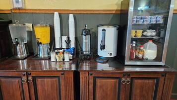 A coffee station with dispensers, cups, and a milk fridge.