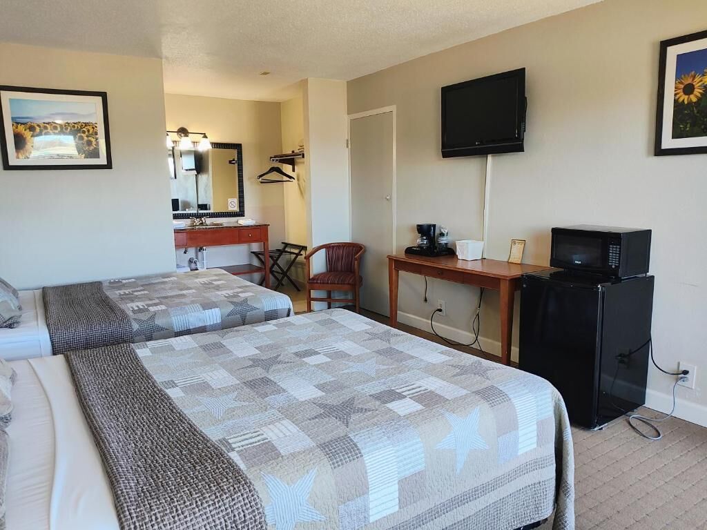 Ett hotellrum med två sängar, ett skrivbord med en dator, en tv och en spegel.