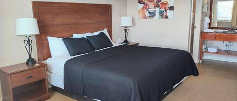 Habitación de hotel con una cama grande, dos mesitas de noche con lámparas, un cuadro en la pared y un baño visible a través de una puerta abierta.
