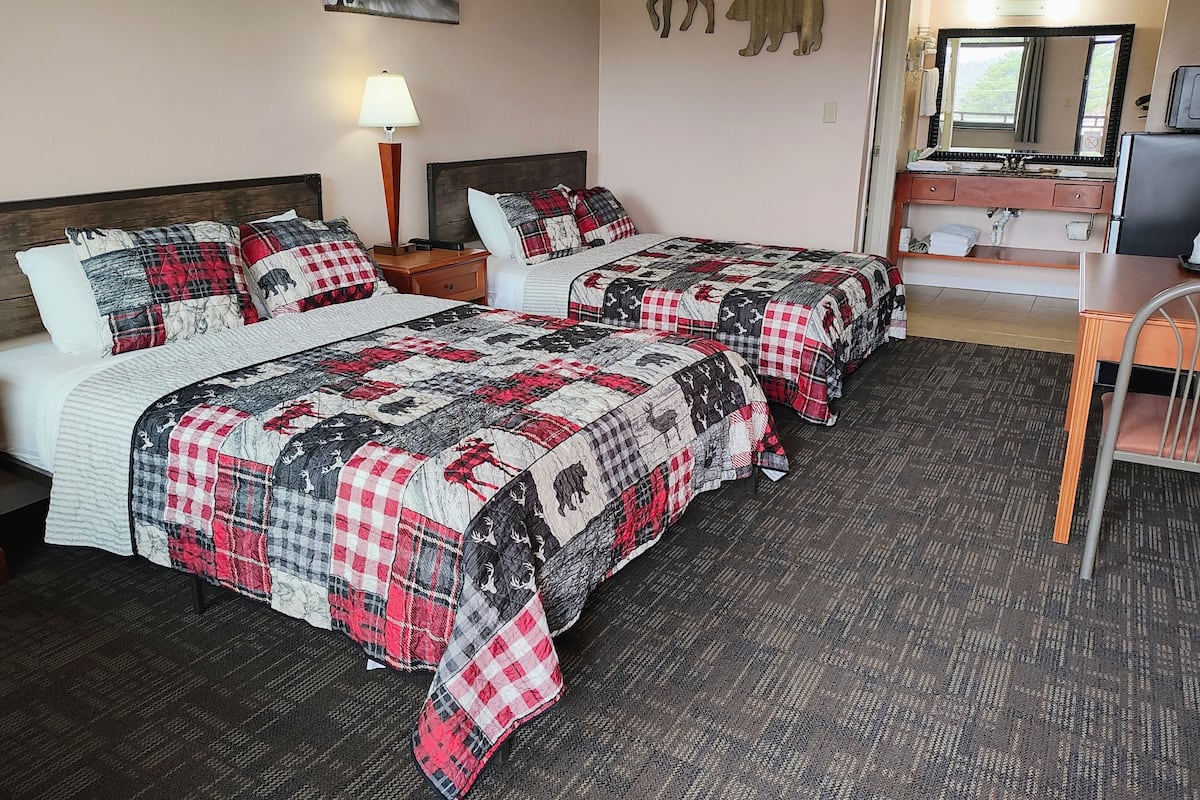 A hotel room with two beds, a desk, a mirror, and a lamp.