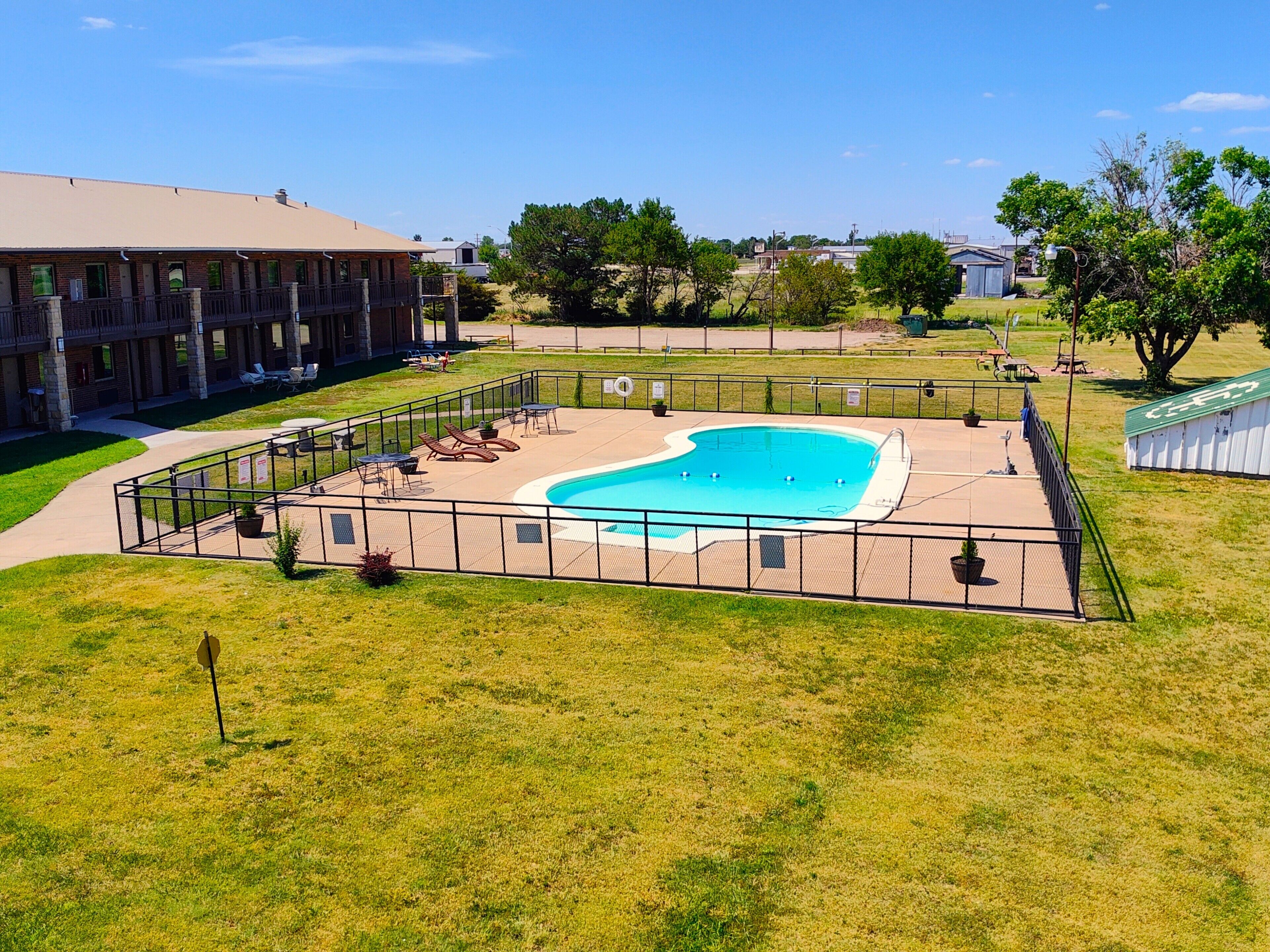 A swimming pool with lounge chairs and a fenced deck area, surrounded by grass and trees.