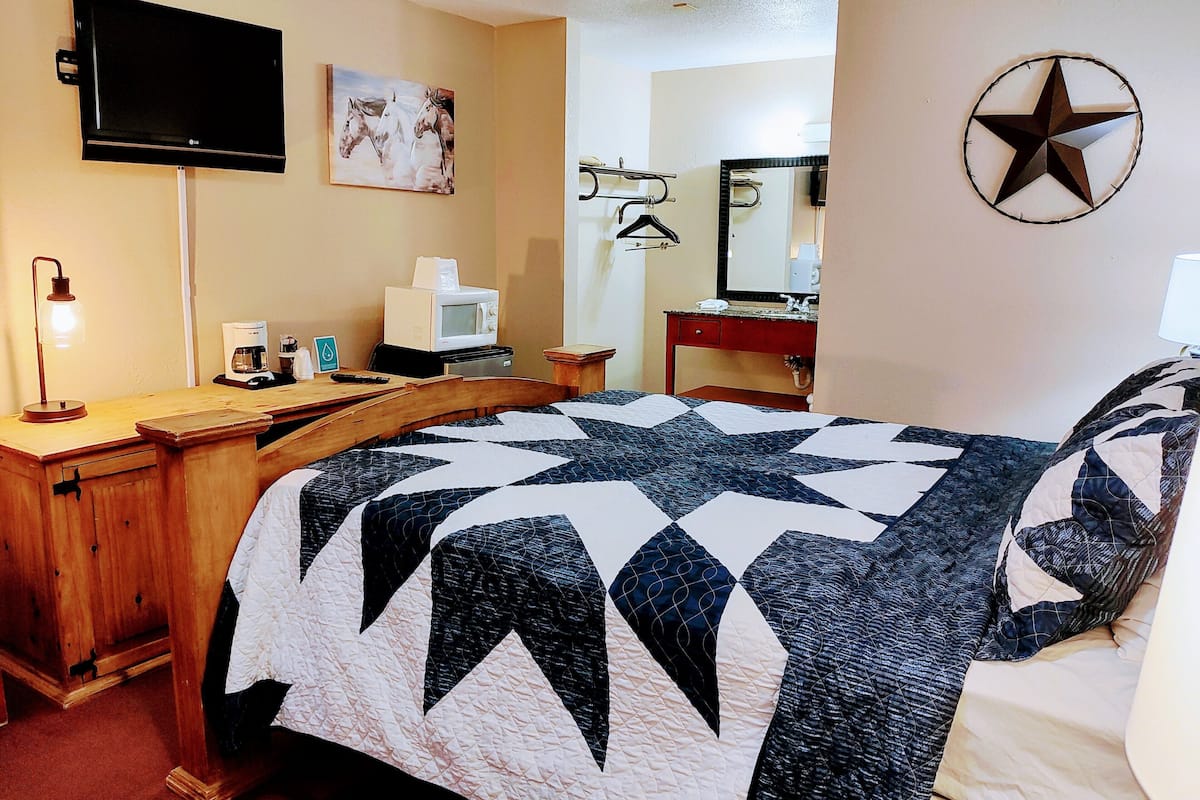 A hotel room with a large bed, a desk with a computer, a flat-screen TV, a coffee machine, and a star decoration on the wall.