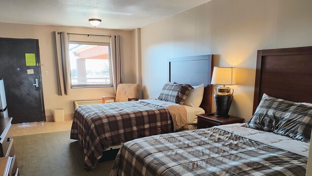 A hotel room with two beds, a desk, a chair, a window with curtains, a lamp, and a door. - The Lodge at Russell (Russell)