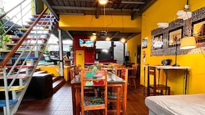 Un comedor con mesas y sillas de madera, una escalera y un sofá.