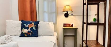 A hotel room with a bed, a nightstand, a lamp, a shelf, and a painting on the wall.