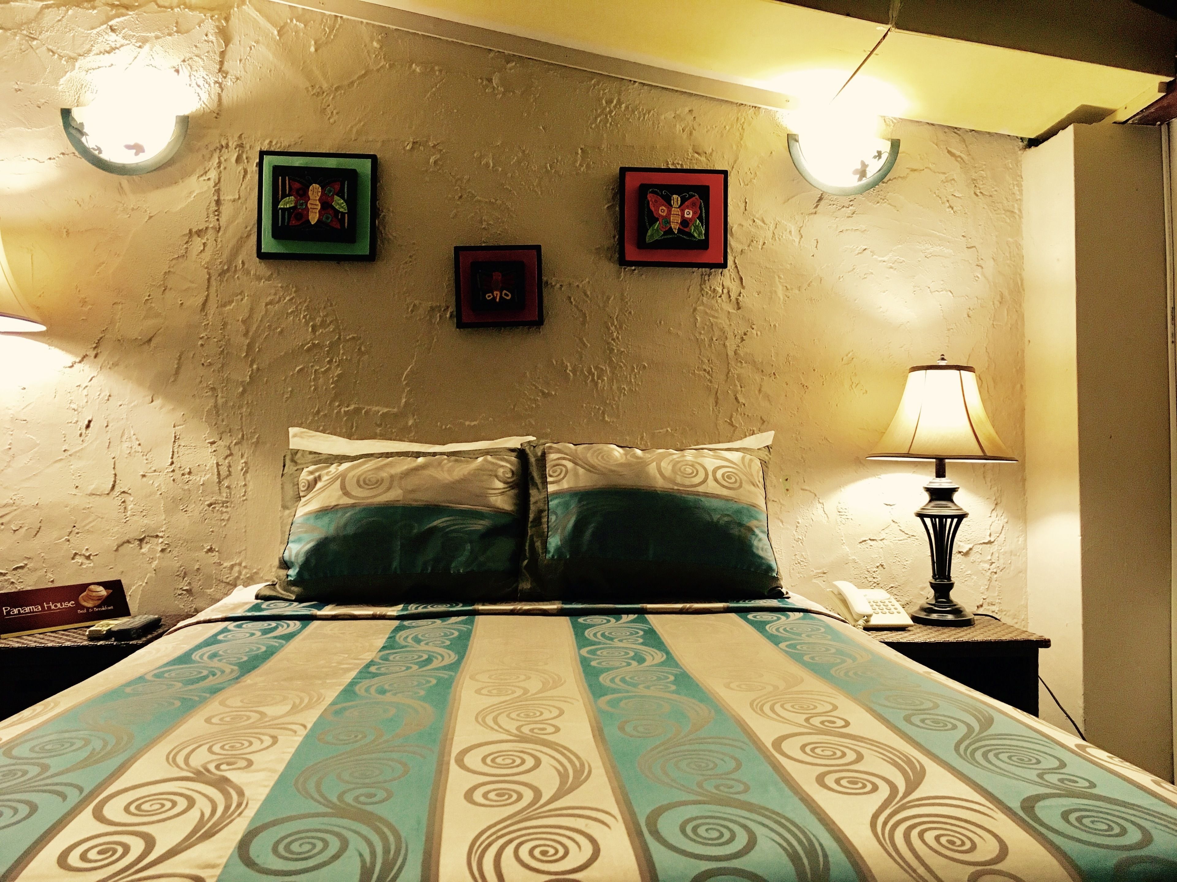 Un dormitorio con una cama, dos almohadas, una mesita de noche con una lámpara y tres cuadros en la pared.