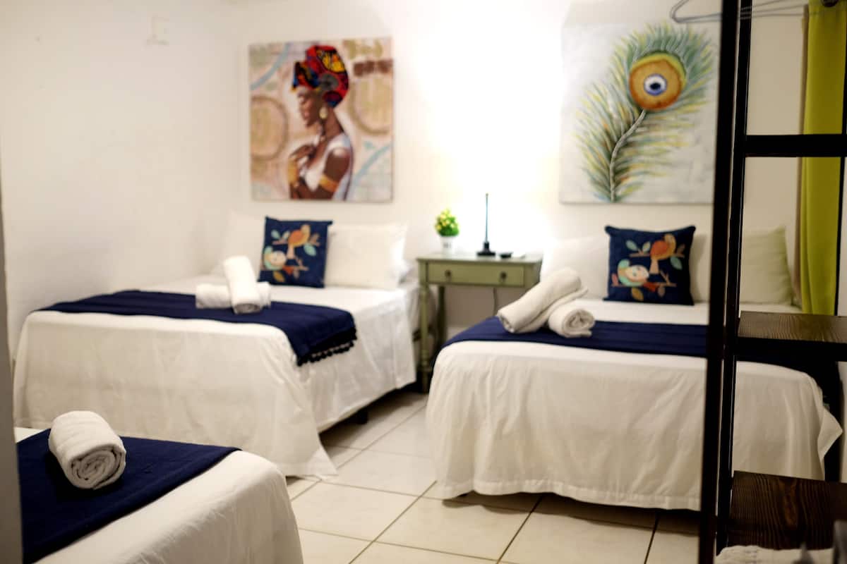 Een hotelkamer met twee bedden, elk voorzien van een witte spreidek en blauwe kussens. Er staat een klein tafeltje met een lamp en een decoratieve plant.
