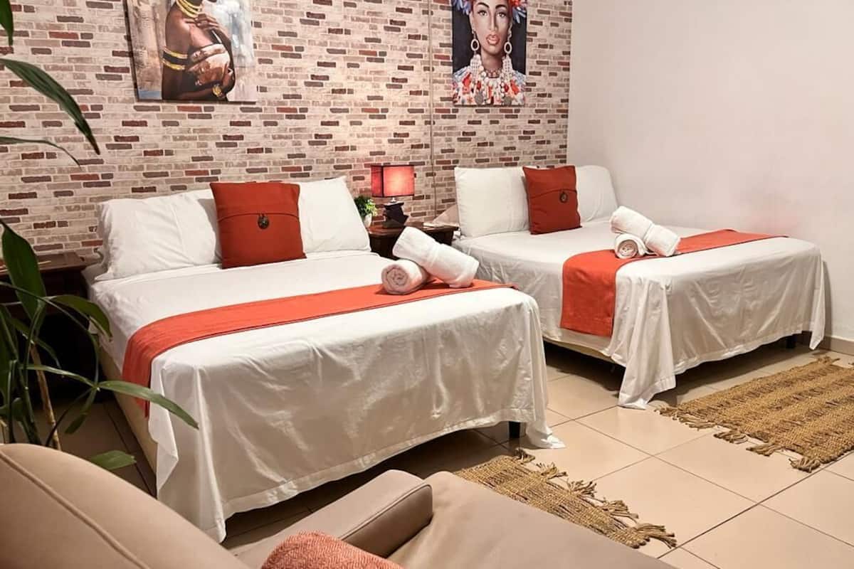 Een hotelkamer met twee bedden, een slaapbank en een bakstenen muur met kunstwerken.