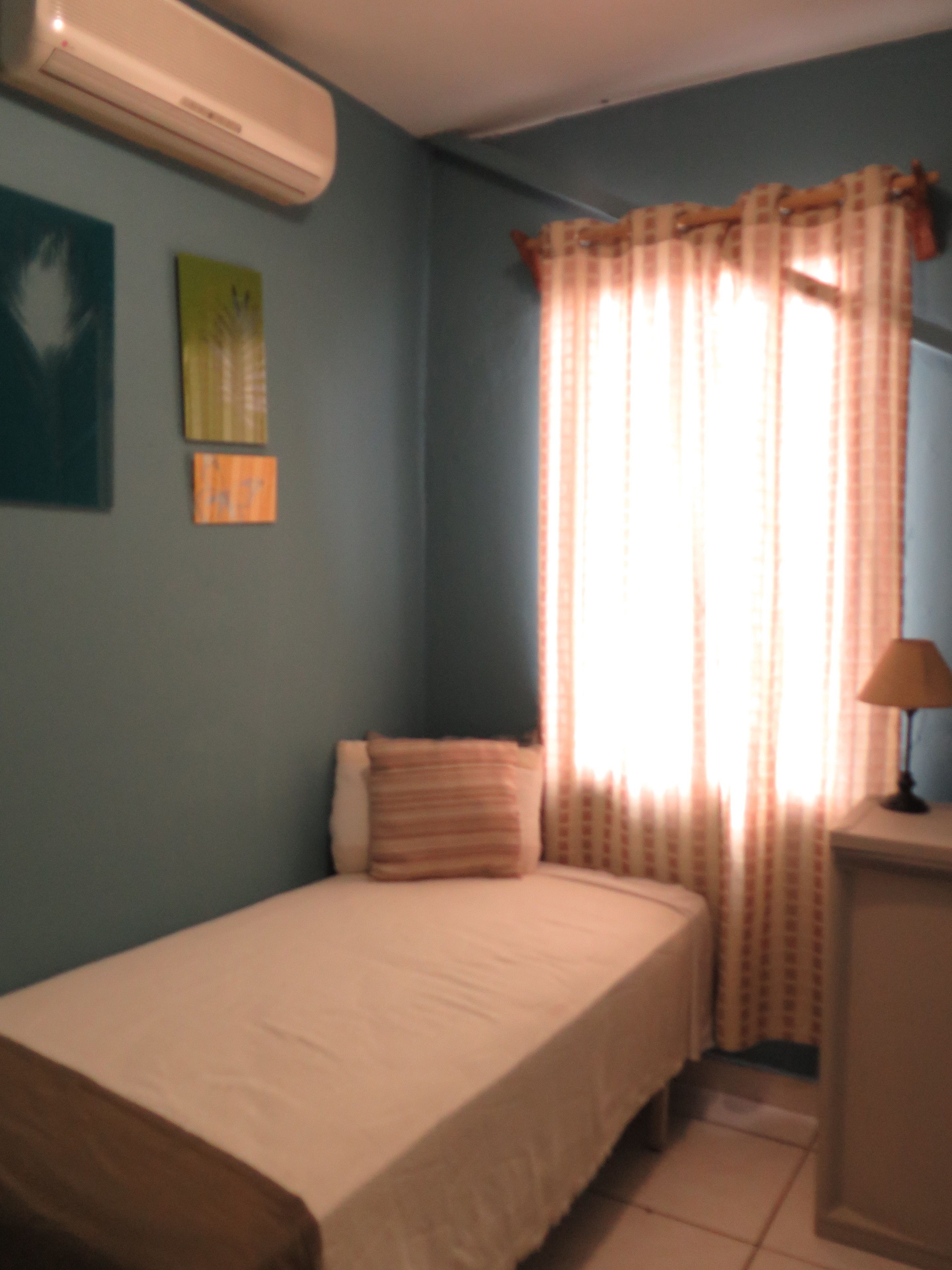 A bedroom with a single bed, a nightstand, a lamp, and a window with curtains.