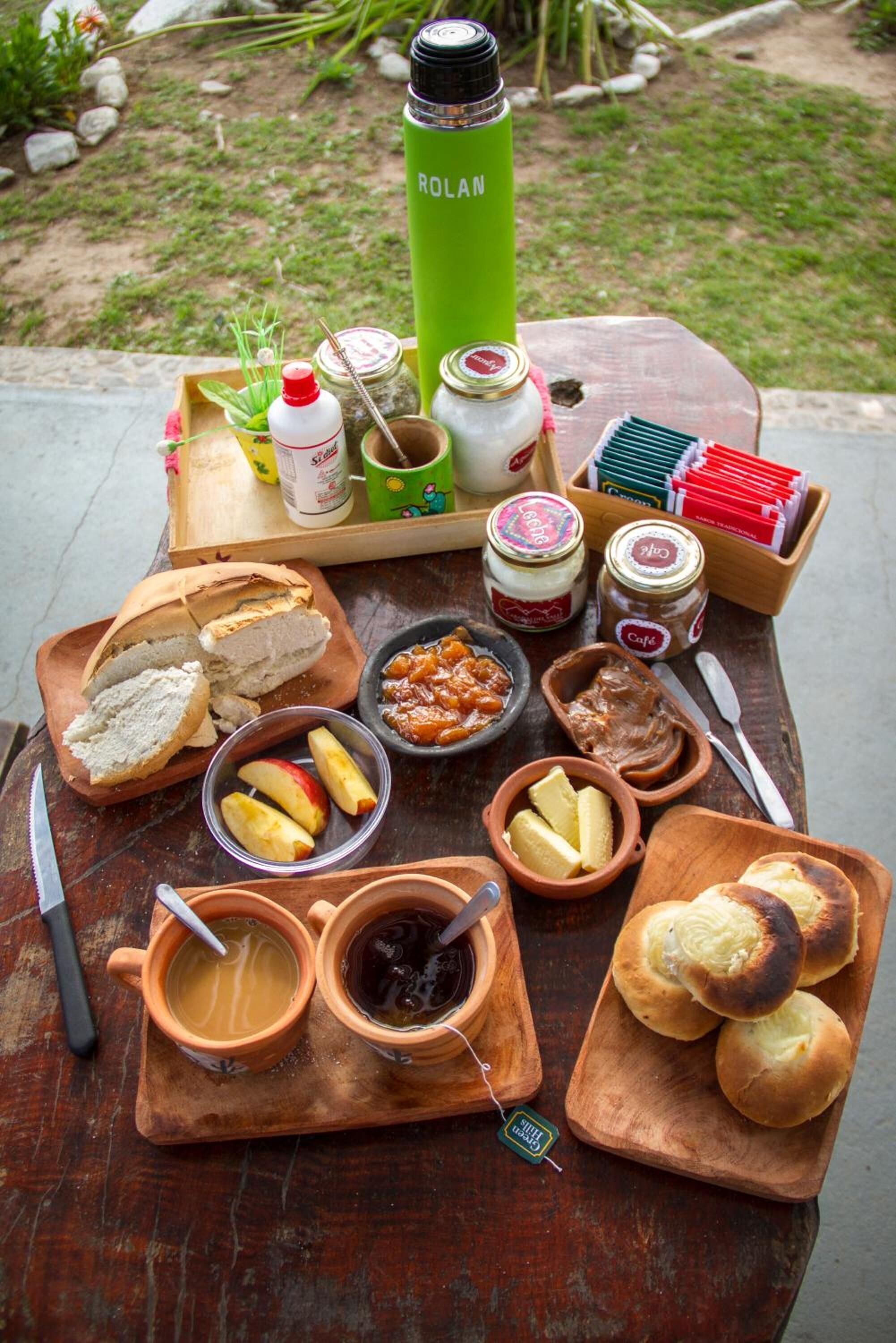 Un montaje para picnic con diversos alimentos y un termo sobre una mesa de madera al aire libre.