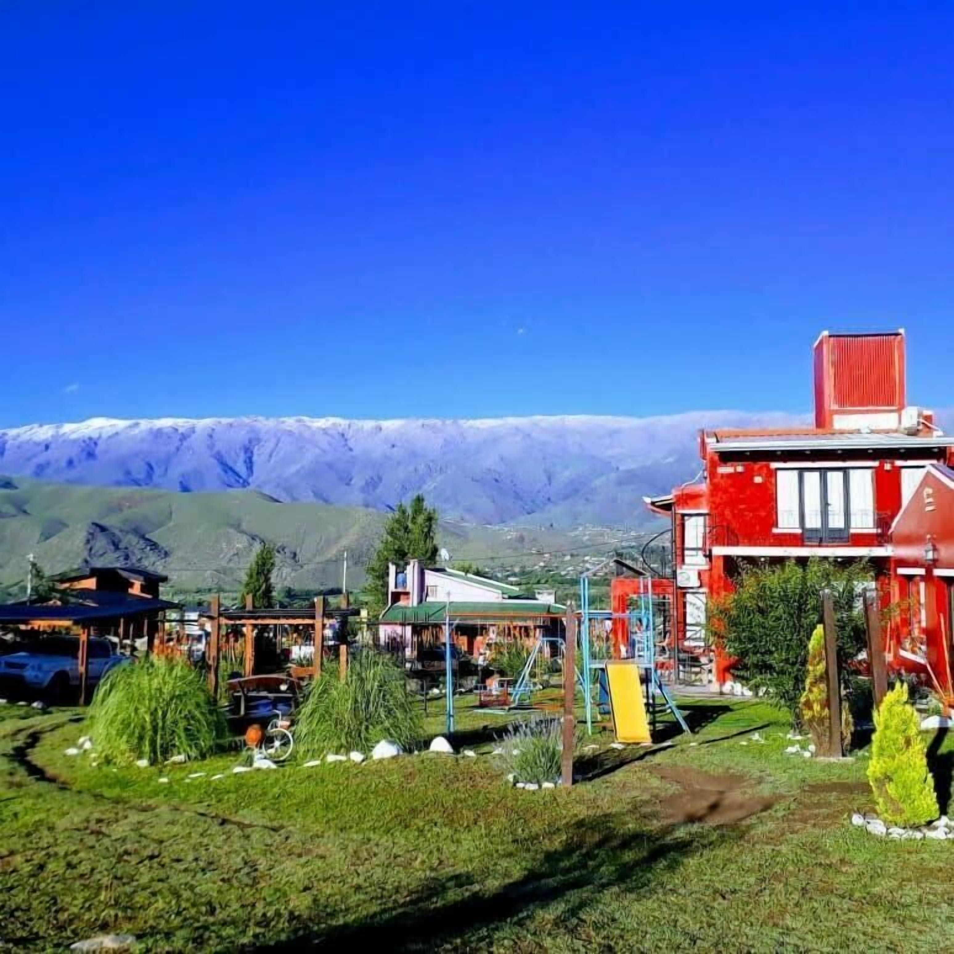 Un edificio rojo con balcón, rodeado de vegetación y montañas al fondo.