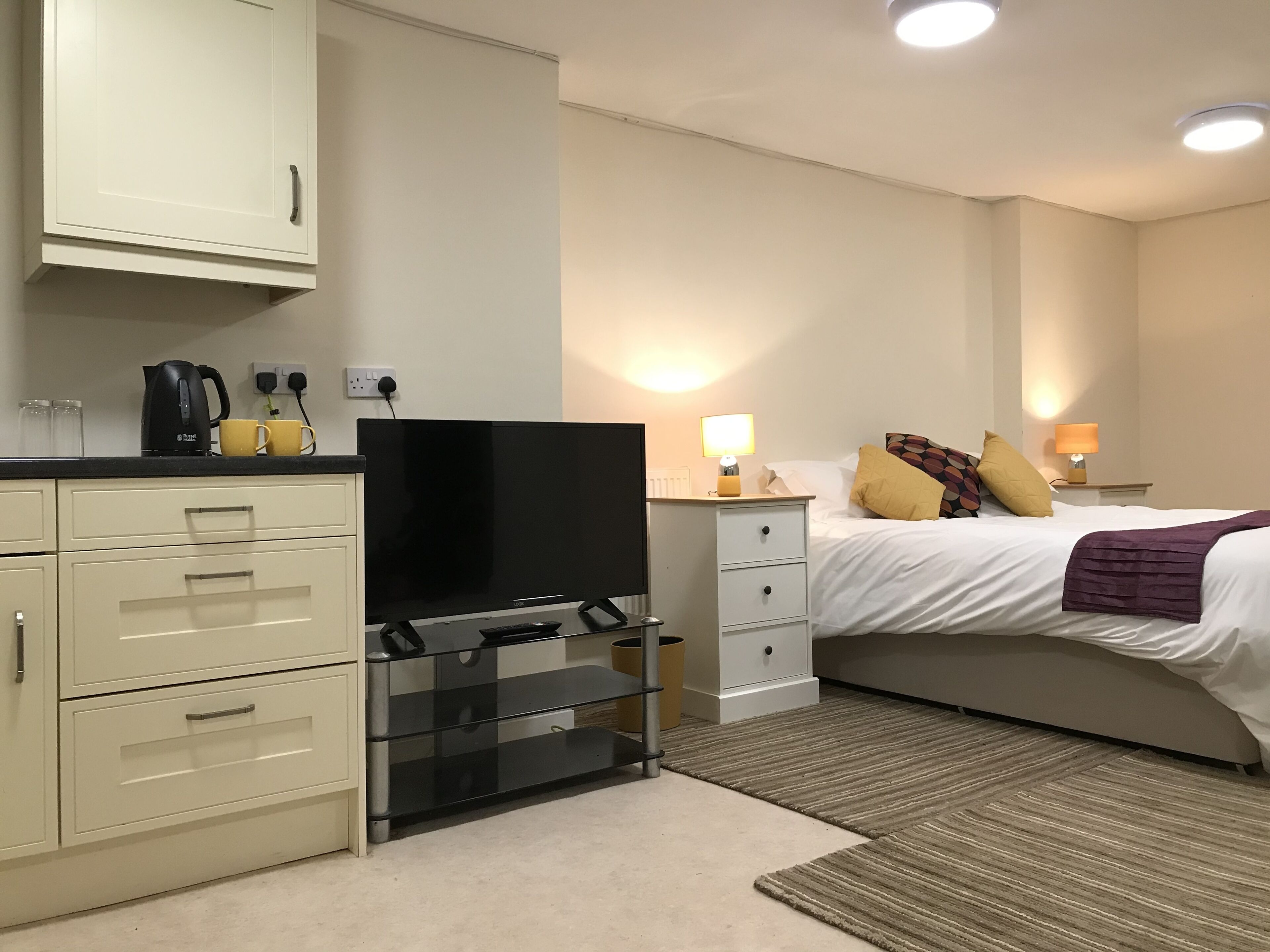 Habitación de hotel con cama, mesita de noche, lámpara y televisor sobre un soporte.