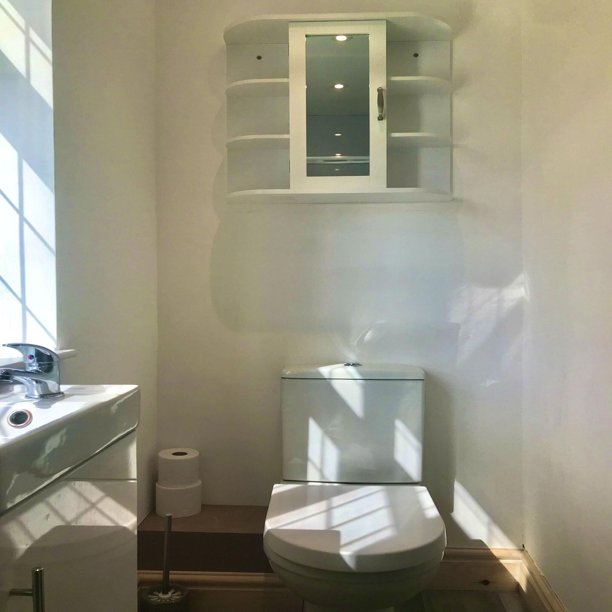 A compact bathroom with a toilet, a sink, and a cabinet above the toilet.