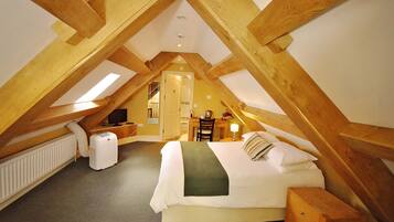 A high-ceilinged attic bedroom with a bed, bedside table, lamp, and a radiator.