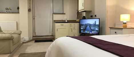 A hotel room with a bed, a television, a desk with a lamp, a radiator, a cabinet, and a door.