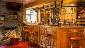 Un rincón de bar acogedor con taburetes de madera, una chimenea de piedra y un televisor montado en la pared.