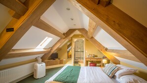 Un dormitorio con techo inclinado, una cama, un radiador, un escritorio y una ventana.