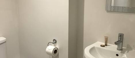 Un baño con inodoro, lavamanos, espejo y cubo de basura.
