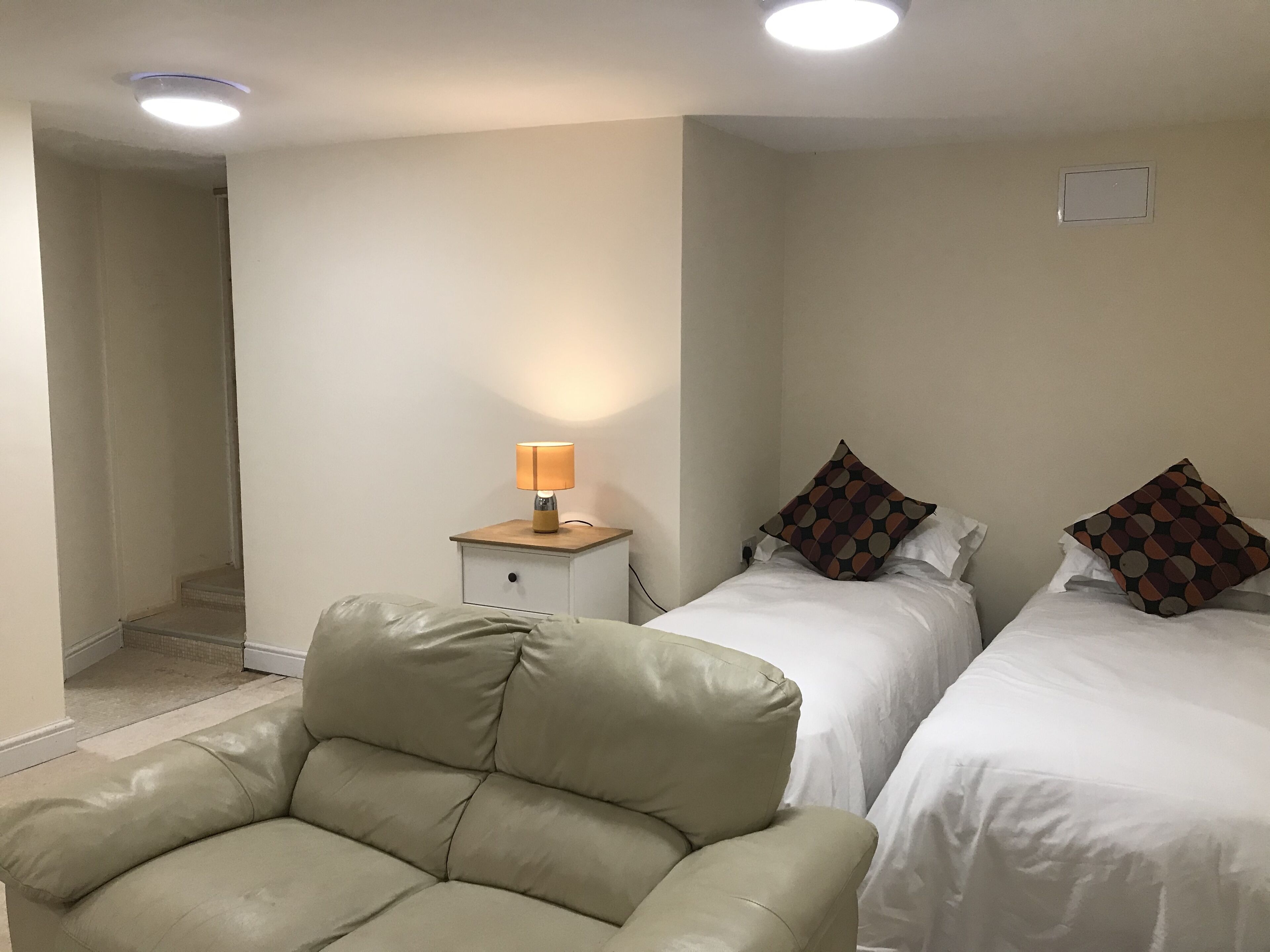 Una habitación con dos camas, una mesita de noche con lámpara y un sillón de cuero.