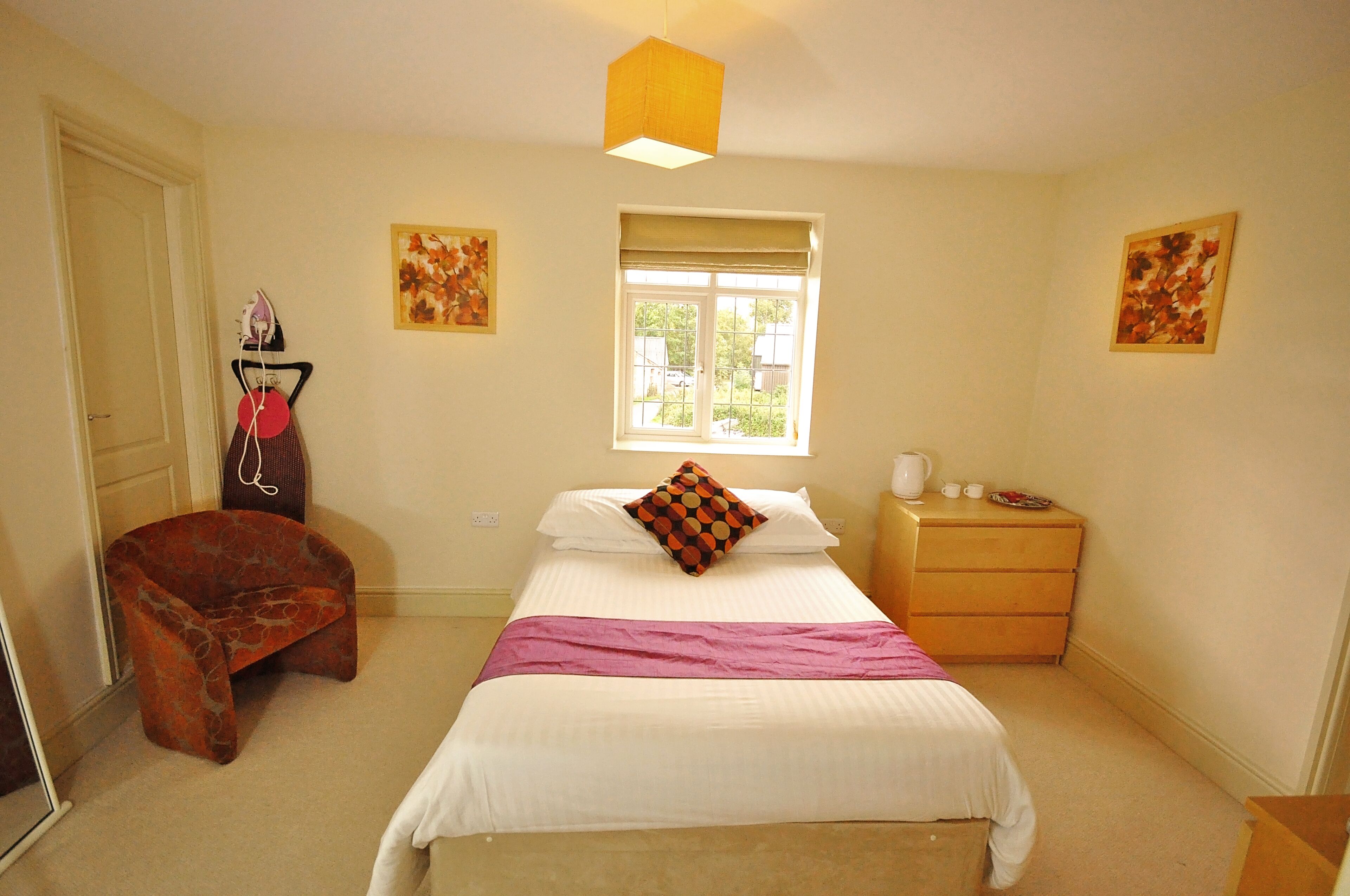 A bedroom with a bed, a chair, a nightstand, a window, and a door.