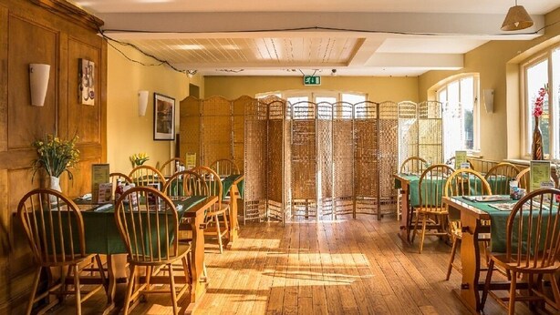 Un comedor con suelo de madera, manteles verdes y sillas de madera.