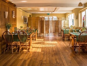 A dining area with wooden flooring, green tablecloths, and wooden chairs. - The Castle Hotel (Brecon)