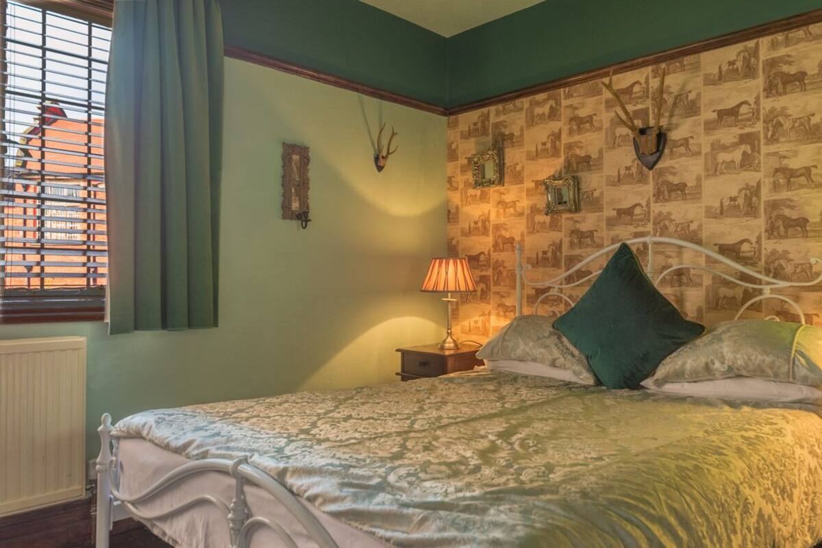 Quarto com cama, duas mesas de cabeceira, abajur e parede com estampas de animais.