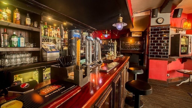 Een bar met flessenkasten vol drank, een toog en krukken.