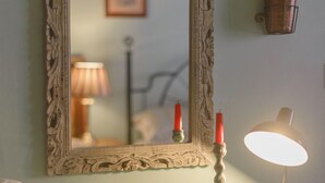 Een spiegel in vintage-stijl met een decoratieve lijst, een kleine potplant, een lamp en een beker met bestek op een dressoir in de kleur teal.