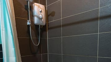 Un espacio de ducha con cabezal de ducha manual, panel de control y desagüe.
